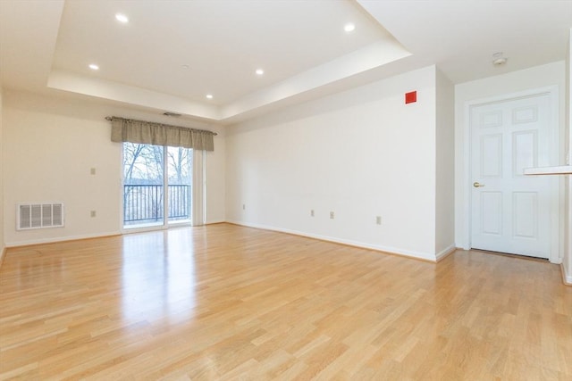 spare room featuring a tray ceiling and light wood-type flooring