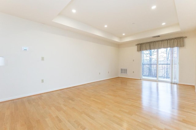 empty room featuring light wood-type flooring and a raised ceiling