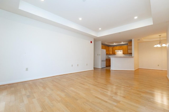 unfurnished living room featuring an inviting chandelier, light wood-type flooring, and a tray ceiling