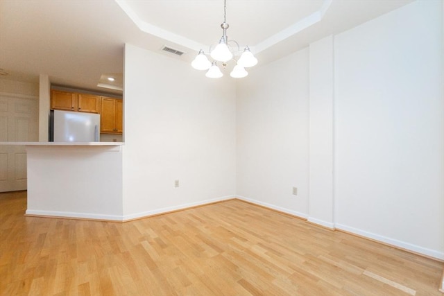 unfurnished room with a tray ceiling, light wood-type flooring, and a notable chandelier