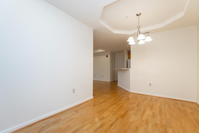 empty room featuring a tray ceiling, an inviting chandelier, and light hardwood / wood-style flooring