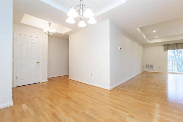 unfurnished room with light wood-type flooring, a raised ceiling, and a notable chandelier