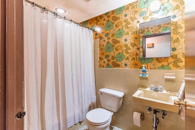 bathroom with a shower with curtain, sink, toilet, a textured ceiling, and tile walls