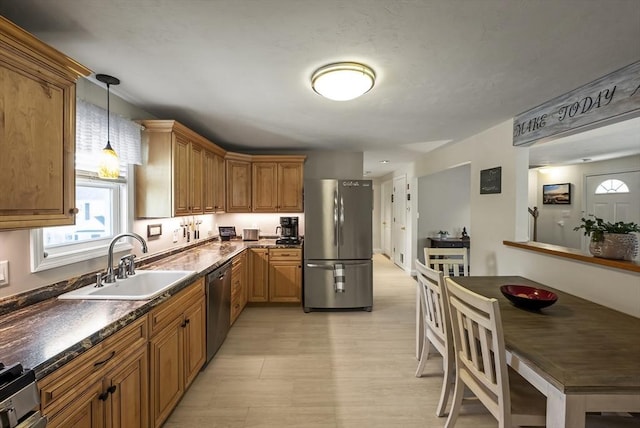 kitchen with stainless steel appliances, a sink, dark countertops, brown cabinetry, and decorative light fixtures