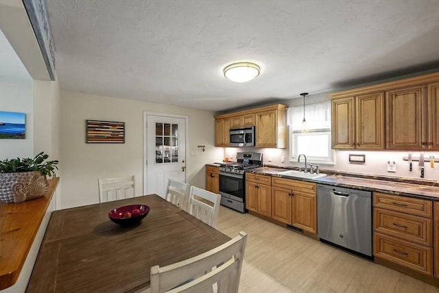 kitchen featuring stainless steel appliances, a sink, brown cabinets, and decorative light fixtures