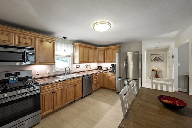 kitchen with appliances with stainless steel finishes, a sink, hanging light fixtures, and brown cabinetry