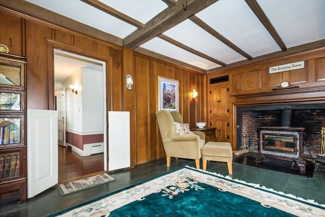sitting room with beamed ceiling, a wood stove, visible vents, wood finished floors, and wood walls