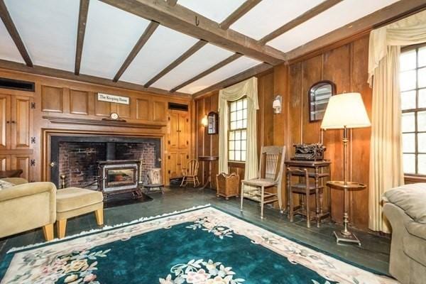 living room with wooden walls, beamed ceiling, and a wood stove