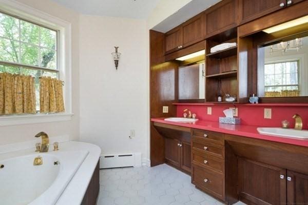 bathroom featuring double vanity, a bath, a baseboard radiator, and a sink