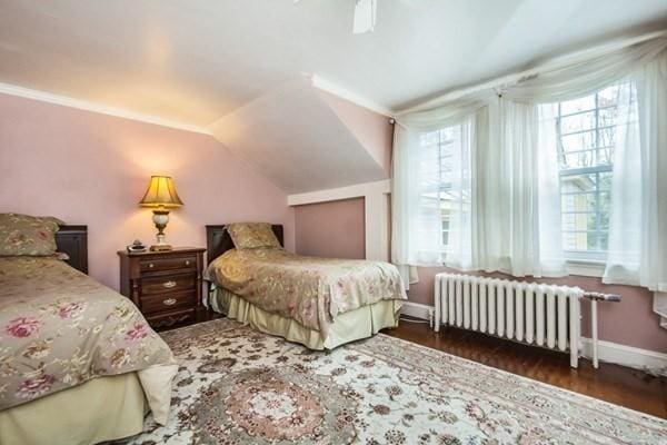 bedroom with radiator, a ceiling fan, vaulted ceiling, wood finished floors, and baseboards