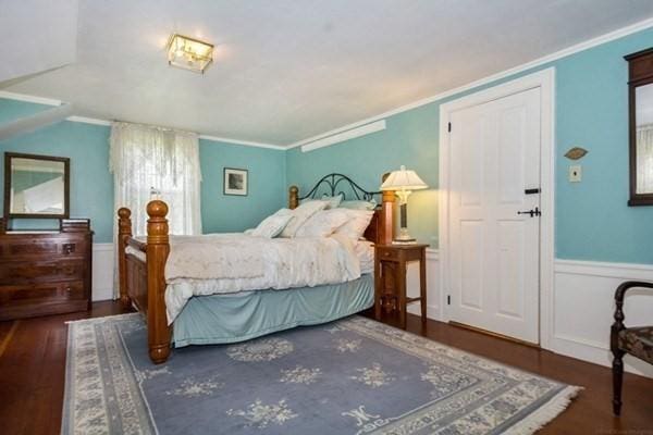 bedroom with crown molding, wood finished floors, and wainscoting