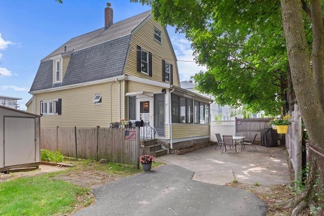 8A 3rd St, Medford, MA 02155 - view of front facade with a gambrel roof, a chimney, a patio area, roof with shingles, and a storage unit