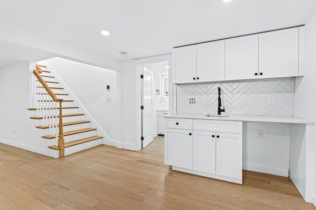 kitchen with light wood-type flooring, backsplash, white cabinetry, and sink