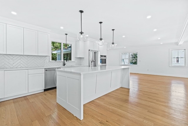 kitchen with white cabinetry, light hardwood / wood-style flooring, decorative light fixtures, a kitchen island, and appliances with stainless steel finishes