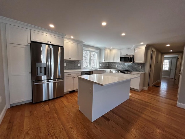 kitchen featuring appliances with stainless steel finishes, hardwood / wood-style floors, a center island, tasteful backsplash, and white cabinets