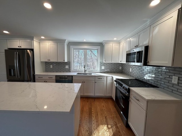 kitchen with sink, wood-type flooring, black appliances, light stone countertops, and white cabinets