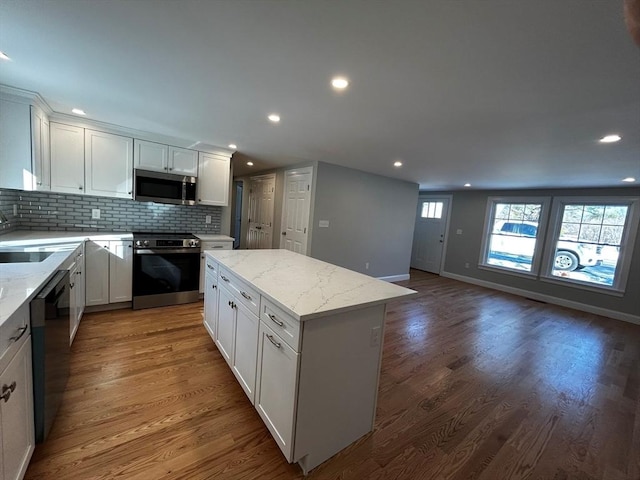 kitchen with a kitchen island, white cabinetry, dark hardwood / wood-style flooring, stainless steel appliances, and light stone countertops