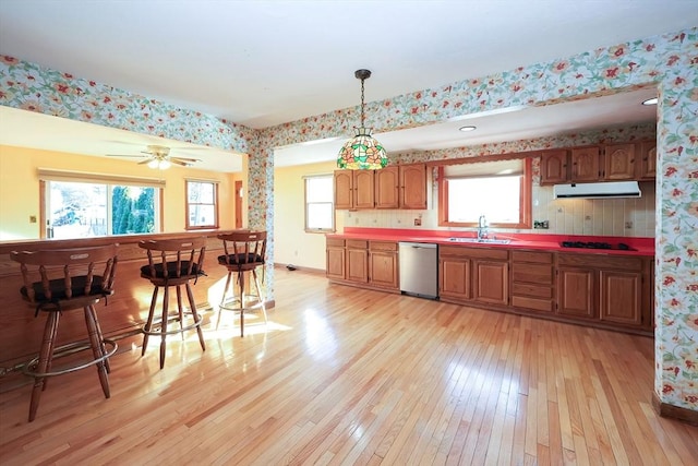 kitchen featuring a breakfast bar, pendant lighting, dishwasher, sink, and light hardwood / wood-style floors