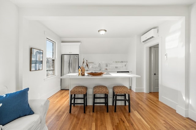 kitchen featuring stainless steel fridge, a kitchen breakfast bar, light wood-type flooring, an AC wall unit, and white cabinetry