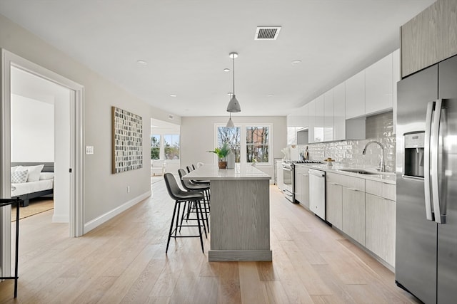 kitchen with hanging light fixtures, sink, light hardwood / wood-style flooring, appliances with stainless steel finishes, and a center island