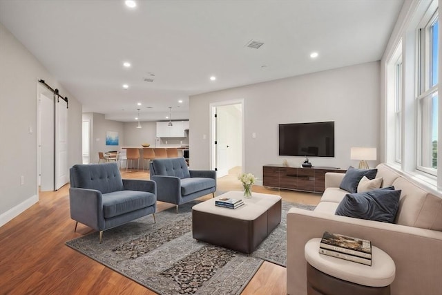 living area featuring visible vents, baseboards, a barn door, recessed lighting, and wood finished floors