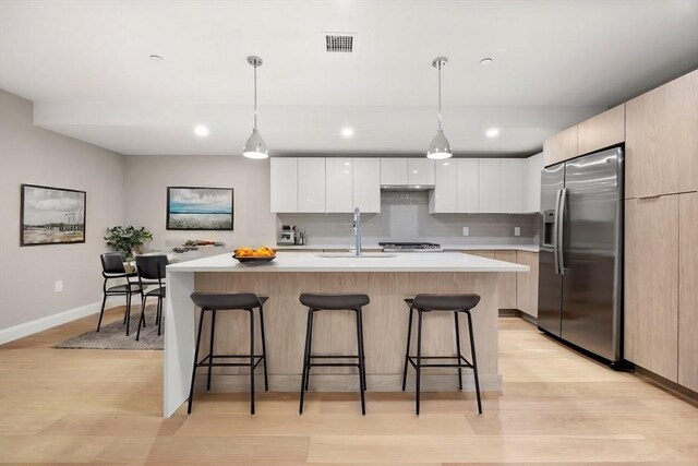 kitchen with a kitchen island, stainless steel appliances, white cabinets, pendant lighting, and light hardwood / wood-style flooring