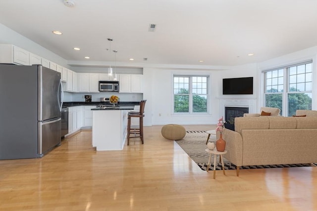 kitchen featuring a fireplace, stainless steel appliances, white cabinets, a kitchen bar, and open floor plan