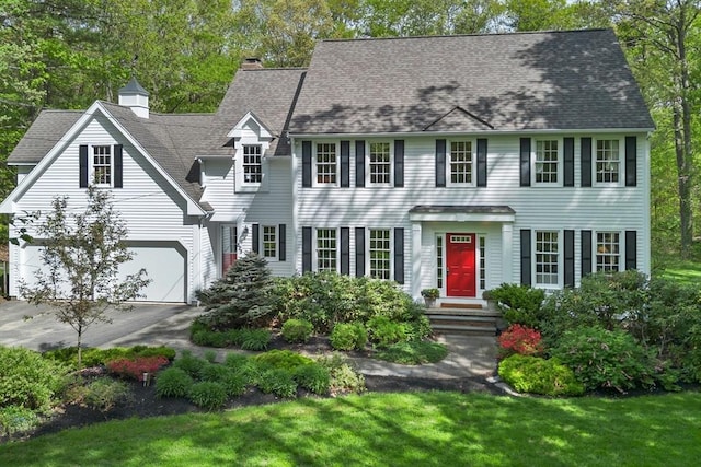 colonial home featuring asphalt driveway, a chimney, a shingled roof, and a front lawn
