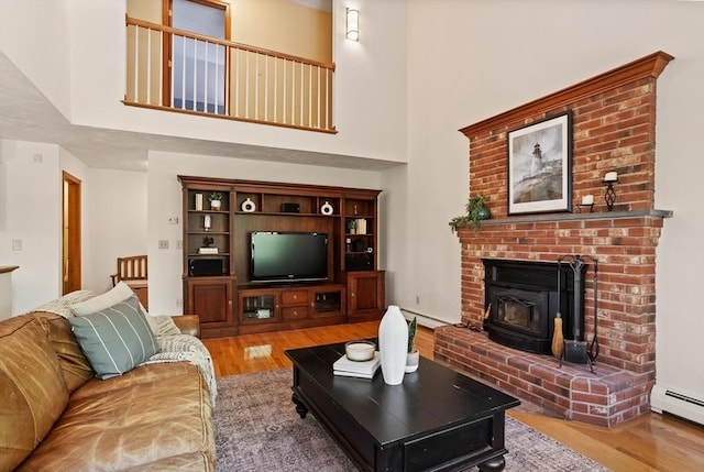 living room featuring wood finished floors, a high ceiling, a baseboard heating unit, and a wood stove