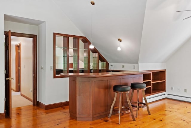 bar area featuring vaulted ceiling, light wood finished floors, a sink, hanging light fixtures, and baseboards