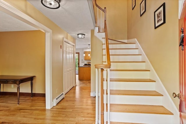 stairs featuring a baseboard radiator, wood finished floors, and baseboards