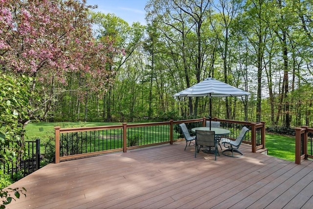 wooden deck featuring outdoor dining area, a lawn, and a view of trees