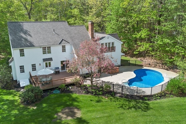 back of property featuring a chimney, a deck, a patio, roof with shingles, and a wooded view