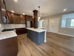 kitchen with dark brown cabinets, a center island, backsplash, pendant lighting, and hardwood / wood-style flooring