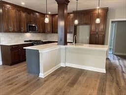 kitchen featuring pendant lighting, wood-type flooring, backsplash, and decorative columns