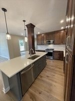 kitchen with stainless steel appliances, sink, pendant lighting, light wood-type flooring, and an island with sink