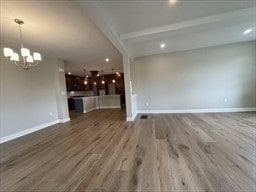 unfurnished living room with an inviting chandelier, beam ceiling, and hardwood / wood-style flooring