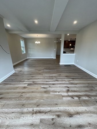 unfurnished living room with an inviting chandelier, beam ceiling, and hardwood / wood-style flooring