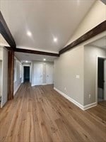 unfurnished living room featuring vaulted ceiling with beams and wood-type flooring