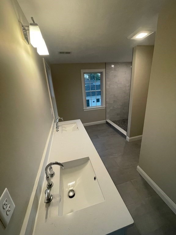 bathroom with a tile shower, dual bowl vanity, and tile patterned floors