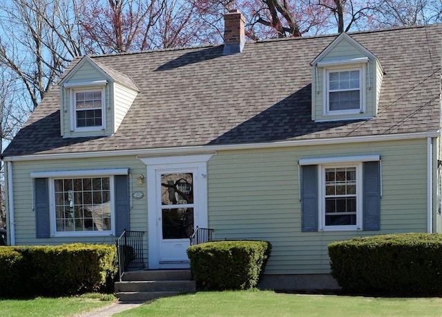 cape cod-style house featuring a shingled roof and a chimney