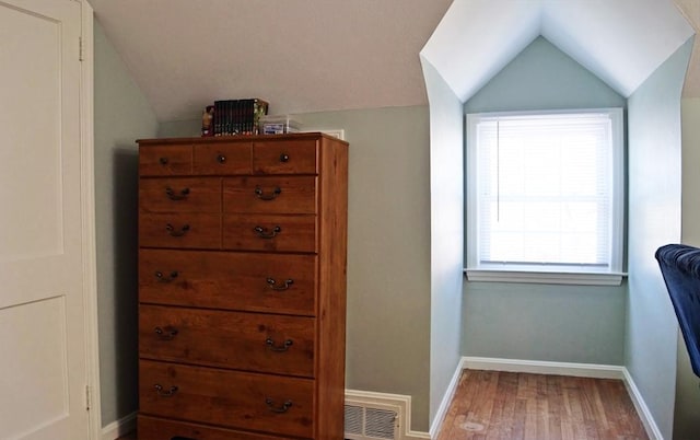 interior space featuring baseboards, lofted ceiling, wood finished floors, and visible vents
