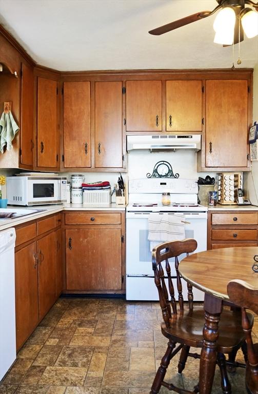 kitchen featuring brown cabinets, ceiling fan, white appliances, light countertops, and under cabinet range hood
