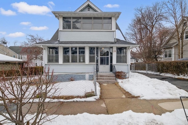 view of front of home with a shingled roof, entry steps, a sunroom, and fence