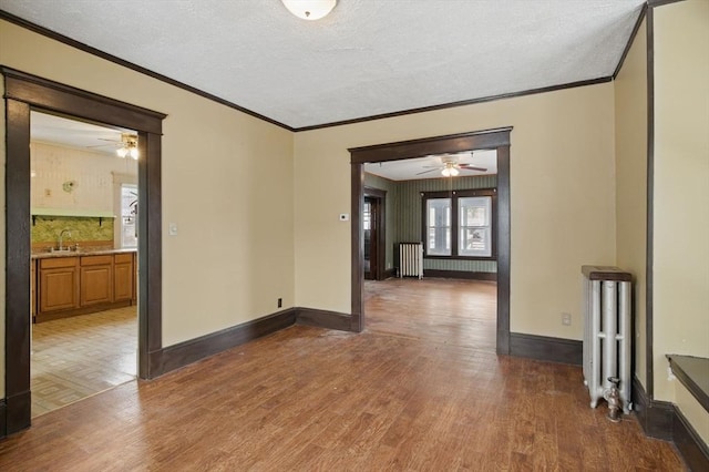 empty room with a sink, radiator heating unit, baseboards, and wood finished floors