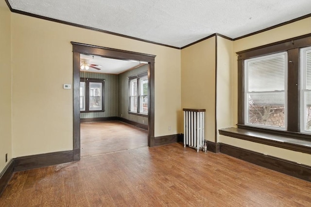 empty room featuring crown molding, a textured ceiling, wood finished floors, and radiator