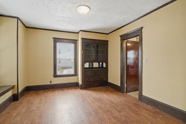 empty room featuring a textured ceiling, baseboards, wood finished floors, and crown molding