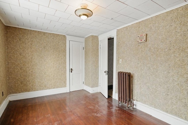 spare room with radiator, wallpapered walls, crown molding, and wood finished floors