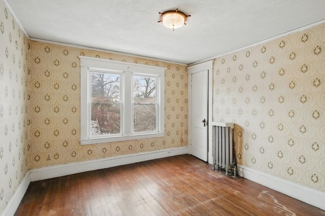 empty room with radiator, wallpapered walls, wood-type flooring, and baseboards