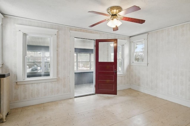 empty room featuring wallpapered walls, a ceiling fan, baseboards, and a wealth of natural light